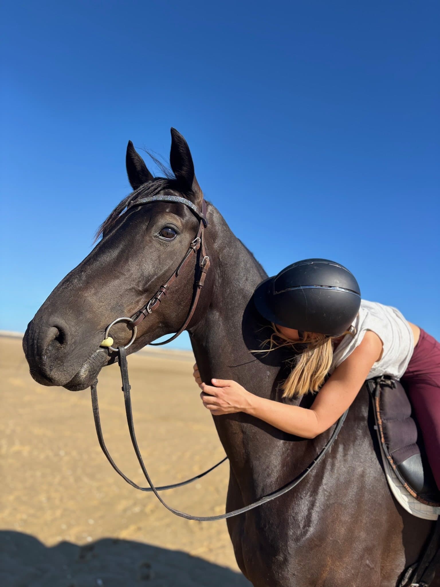 A rider leaning down to hug a dark horse on the beach